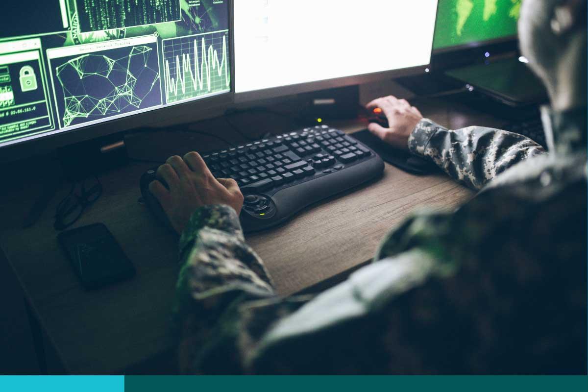 Navy personnel working typing on a keyboard in front of a large computer screen showing data ad graphs