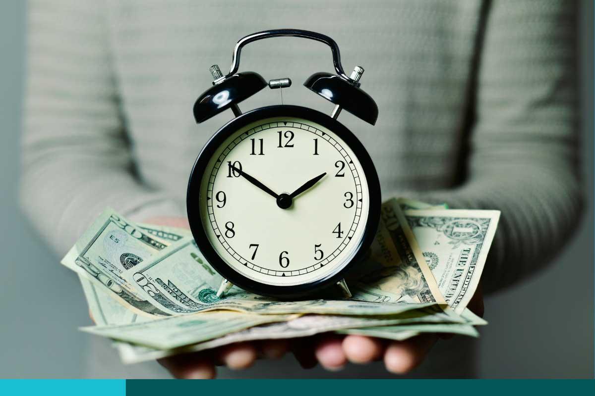 Man holding an analog alarm clock on a pile of money in his outstretched hands