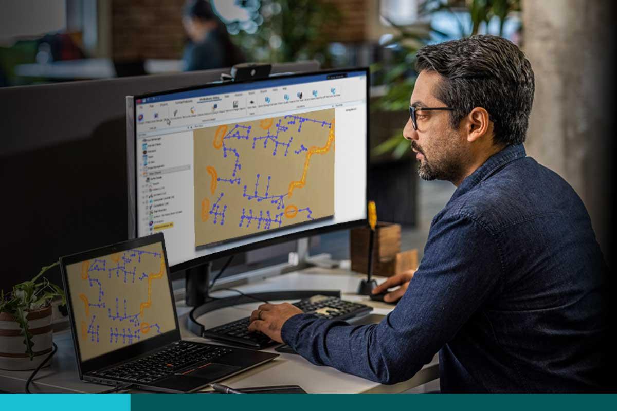 Man working on a graphic of water lines on a laptop with a second monitor